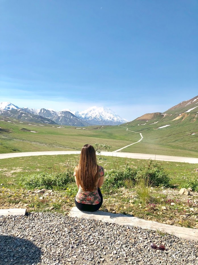 Picture of me sitting in front of a mountain in Alaska, which is a great summer babymoon destination. 